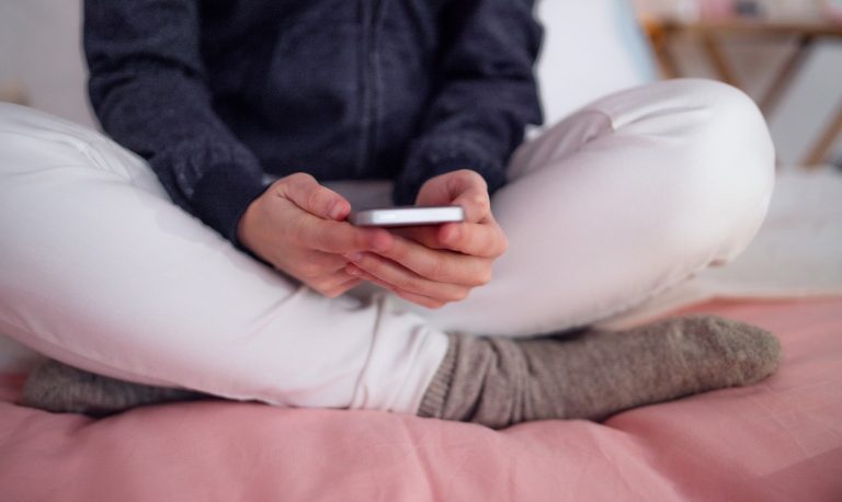Midsection of young girl with smartphone indoors, internet abuse concept