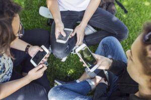 High angle view of teenage girls and teenage boy sitting on grass and using smart phones High angle view of teenage girls and teenage boy sitting on grass and using smart phones