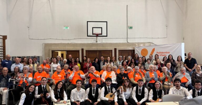 Group portrait in a gym: seniors in orange shirts seated in front with student musicians in formal attire kneeling at the front; banner reads Politécnico de Viseu on the right.]','Large crowd of seniors in orange shirts posing with younger musicians in front of a school gym; basketball hoop visible in the background; banner Politécnico de Viseu on the right.','Multi-generational group photo at a school event in a gym, featuring elderly volunteers in orange shirts and a row of young musicians in white shirts and black vests in front.','Group photo inside a gymnasium showing an audience in bright orange shirts and a band of young musicians in front; a banner for Politécnico de Viseu is visible.','Crowd shot from a school event: elderly participants in orange shirts with a performance group of students in front, banner reading Politécnico de Viseu on the side.