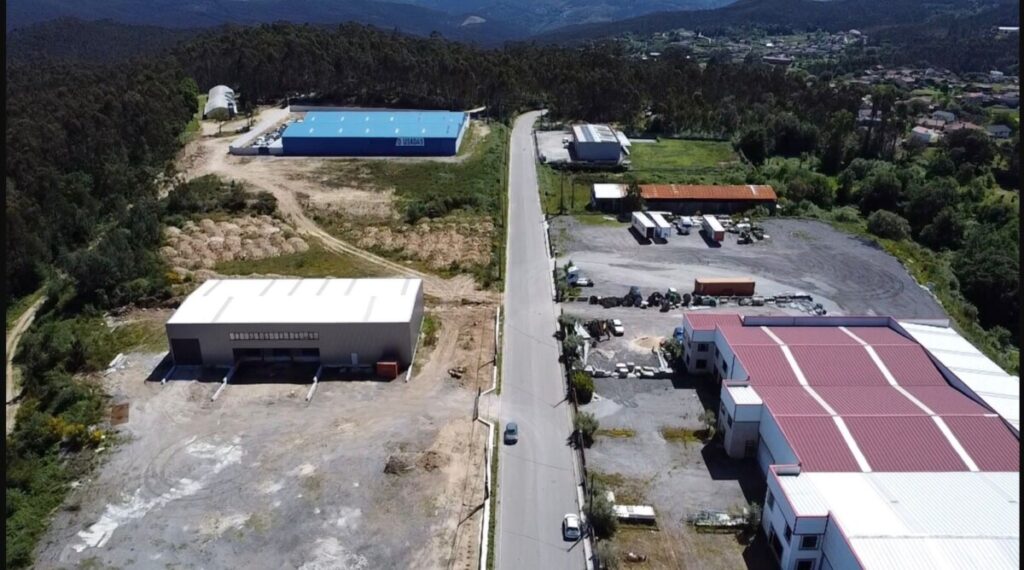 Aerial view of an industrial complex along a central road, with white- and blue-roofed warehouses and surrounding trees and fields. Alteração ao PDM de Oliveira de Frades entra em consulta pública