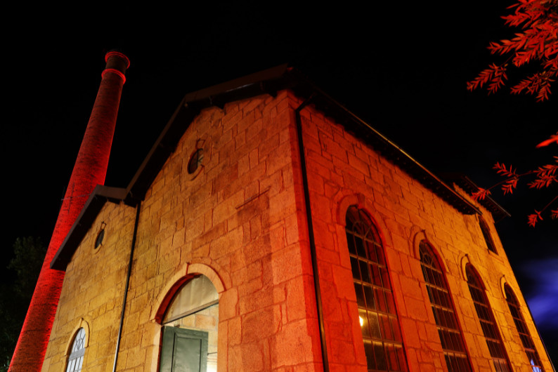 Night photo of a stone church bathed in red light, with a tall chimney on the left and arched windows on the facade. Museu da Eletricidade de Viseu no Campo de Viriato vai ser recuperado para uso cultural