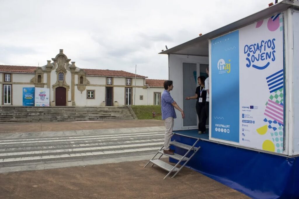 Two people on a blue mobile stage trailer converse outside a historic building with steps and a crosswalk in the foreground. Castro Daire: Jovens querem integrar debate de políticas e deixarem de ser meros destinatários