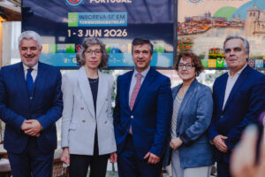 Group of five professionals in business attire posing for a photo at a tourism event with a banner behind them reading dates in June 2026.