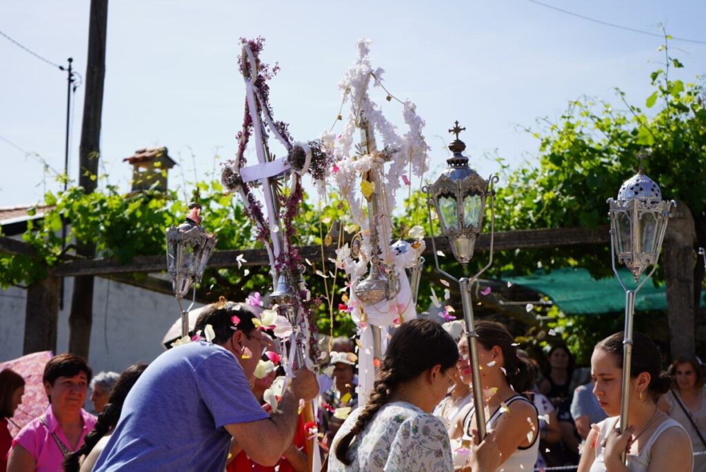 Outdoor religious procession with people carrying ornate crosses and lanterns adorned with flowers under a sunny sky. Festa das Cruzes do Guardão regressa este sábado com séculos de tradição e devoção