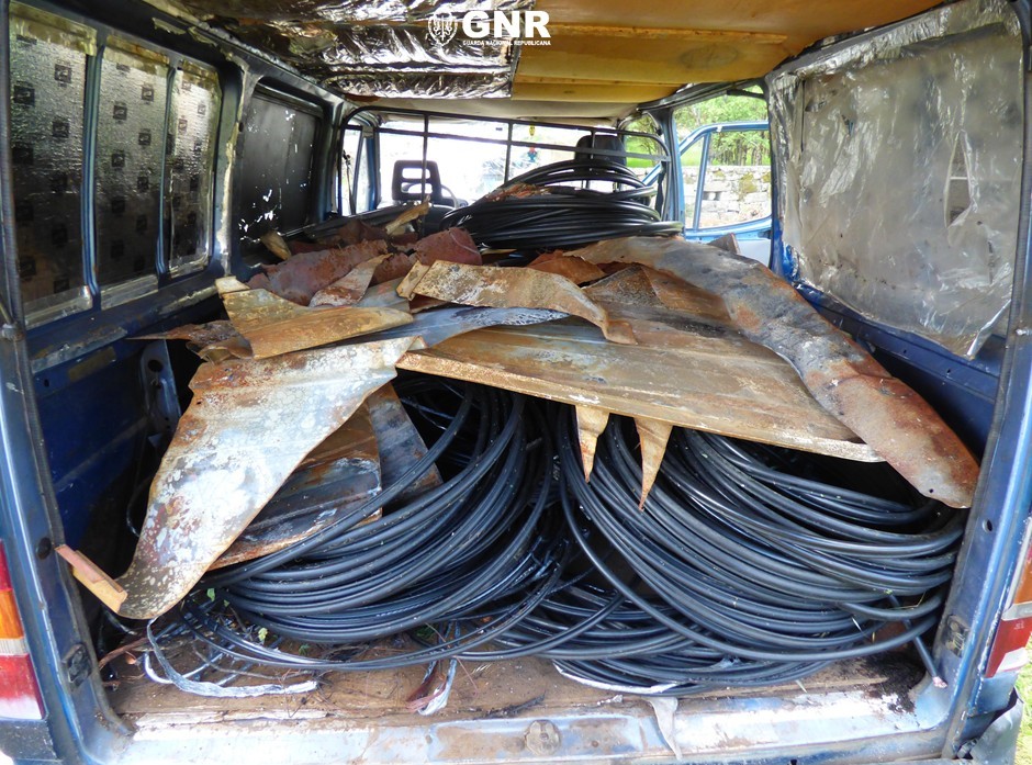 Back of a blue van filled with coiled black cables and rusted corrugated metal sheets in a cluttered cargo area. GNR deteve três homens quando cortavam linha telefónica para furtar fios de cobre