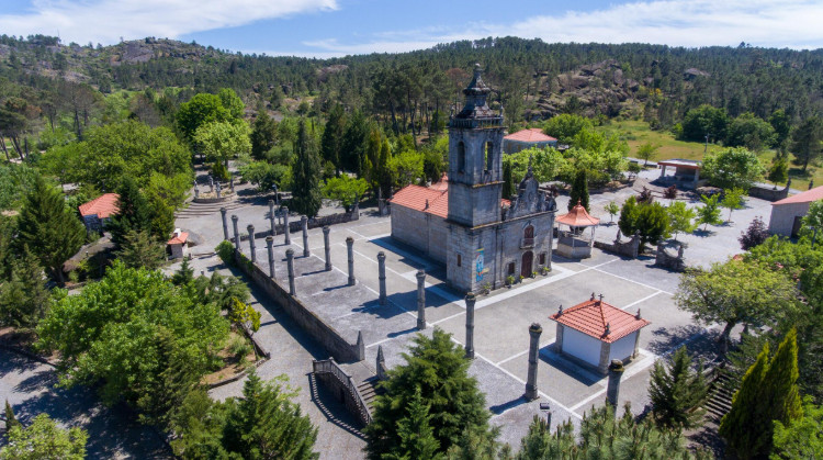 Stone church with a bell tower in a rectangular plaza surrounded by columns in a hillside park.