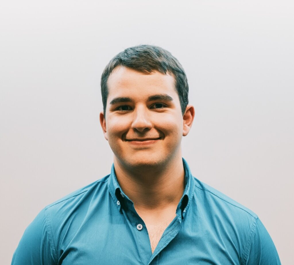 Smiling man in a teal button-down shirt against a light gray background, for a professional headshot