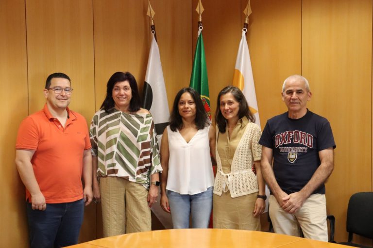 Five adults stand side by side in a wood-paneled room with three flags behind them, smiling at the camera.