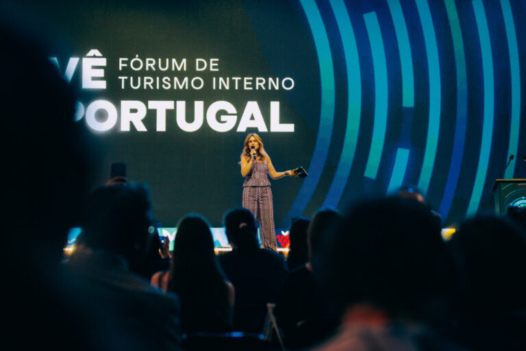 Female presenter on stage speaking at the Fórum de Turismo Interno Portugal with a large 'PORTUGAL' display behind her.