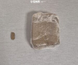 Brown rectangular block wrapped in plastic on a light surface, with a small piece to its left.
