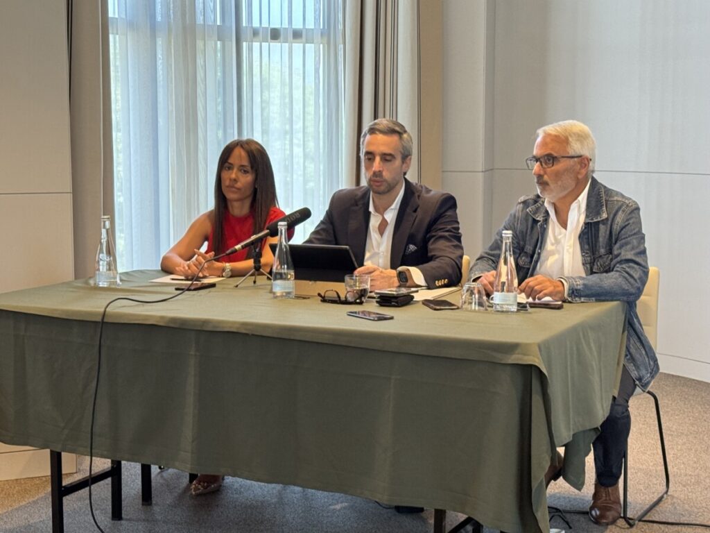 Three adults seated at a conference table with microphones, speaking at a panel briefing. Associação José Junqueiro nasce em Viseu com foco na juventude e sentido crítico