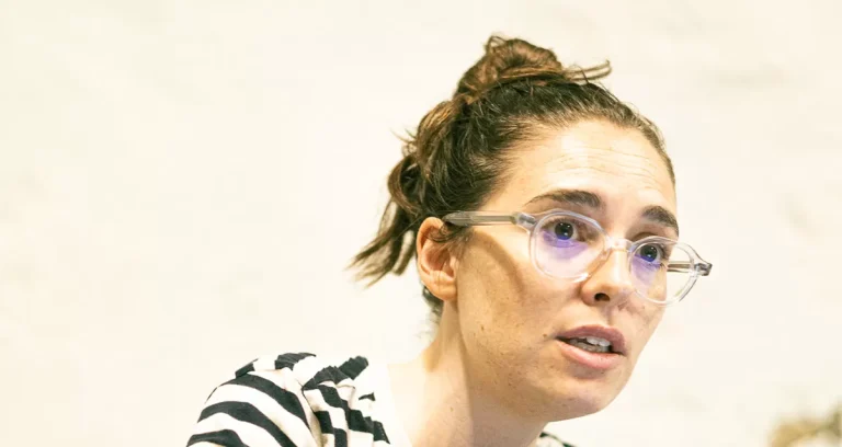 Woman with brown hair in a bun wearing clear glasses, looking to the side in a striped top.