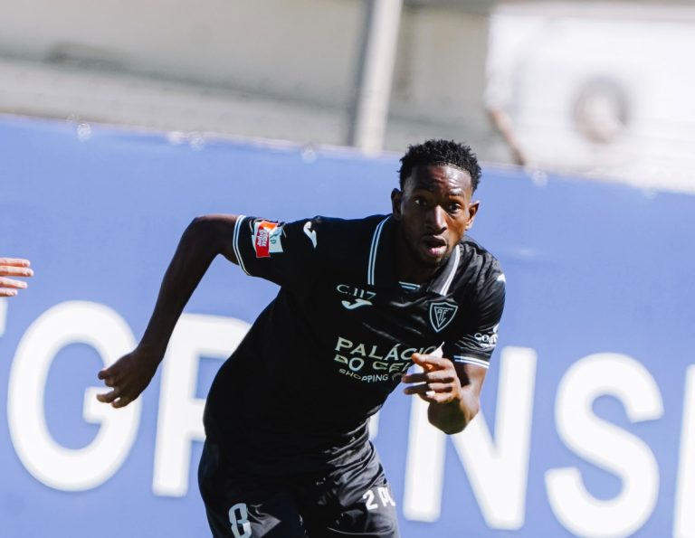 Soccer player in a black jersey sprinting on the field during a match, number 6 visible on shorts, blue advertising boards in the background