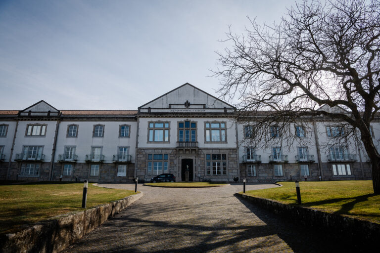 Front view of a large white historic building with a central entrance and stone base, a gravel path leading to the door, and a leafless tree on the right.