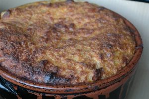 Clay pot dish with a golden-brown bubbly cheese crust on top, likely baked casserole or pot pie served in a terracotta cocotte.