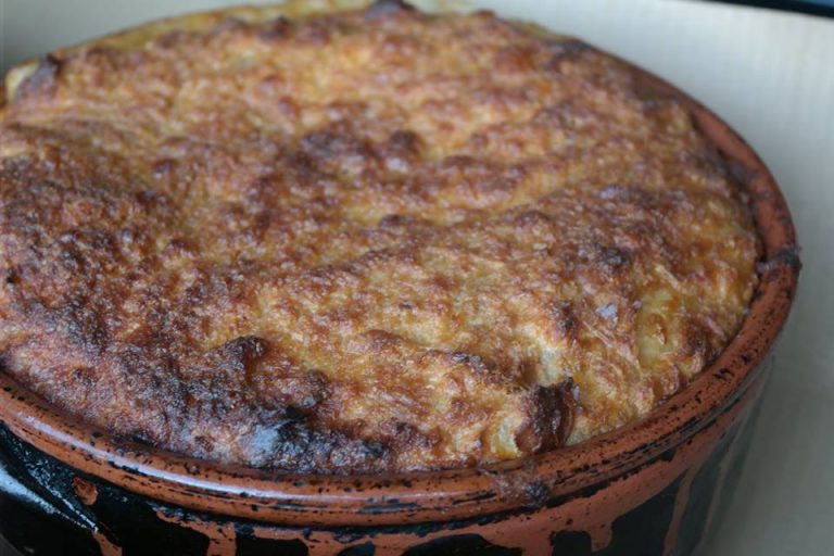 Clay pot dish with a golden-brown bubbly cheese crust on top, likely baked casserole or pot pie served in a terracotta cocotte.