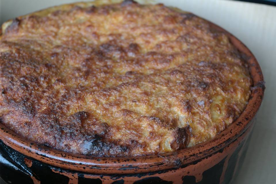 Clay pot dish with a golden-brown bubbly cheese crust on top, likely baked casserole or pot pie served in a terracotta cocotte. Alcofra celebra tradição gastronómica com a 11.ª Mostra da Sopa Seca