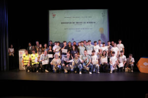 Group of students and mentors on a stage posing with certificates after a business ideas competition ceremony, with a large screen backdrop behind them.