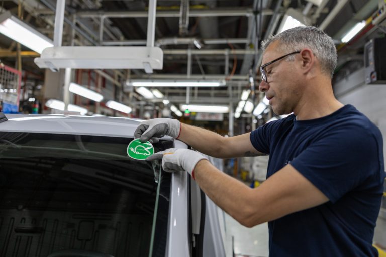 Worker applies a green circular car sticker to the windshield of a white van in an industrial workshop.