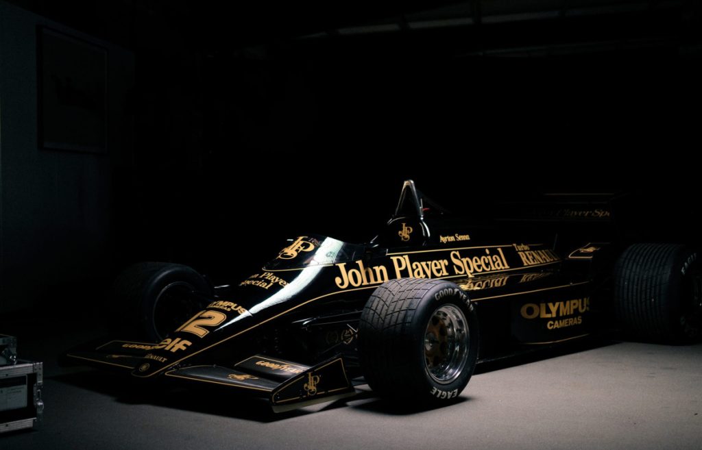 Vintage black John Player Special Formula 1 car in a dim showroom, gold lettering prominently displayed along the body. Exposição dedicada à Fórmula 1 no Museu do Caramulo com carros de Ayrton Senna e Schumacher