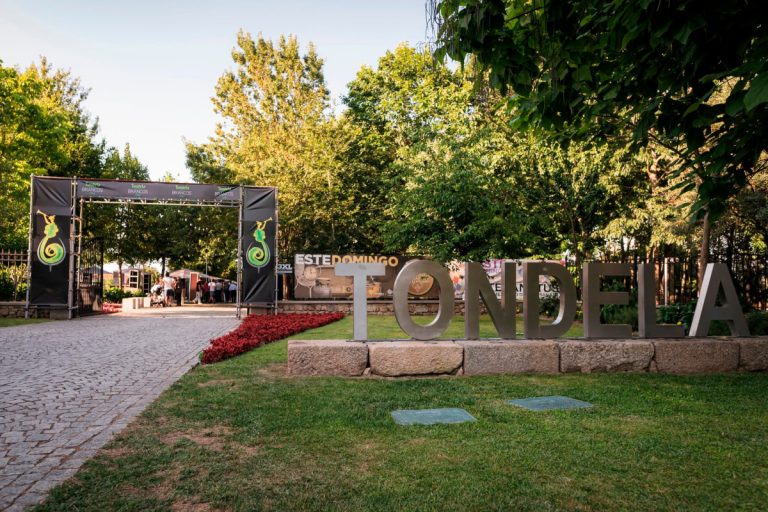 Entrance to an outdoor festival with large metal letters spelling TONDELA on a stone base, trees and a cobblestone path nearby.