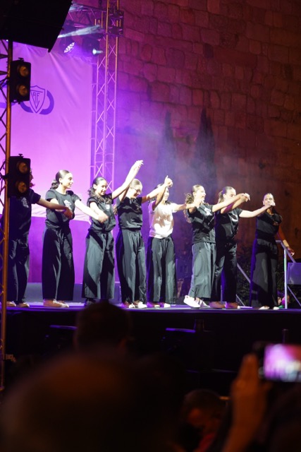 Nine dancers in black on a stage performing a synchronized routine under purple stage lights. Académico de Viseu com plantel “coeso e humilde” no regresso à I Liga, 37 anos depois