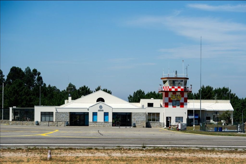 Small regional airport with a white terminal and a red-and-white checkered control tower against a blue sky. Viseu Dão Lafões aposta em Estratégia para a Economia da Defesa