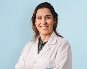 Smiling female healthcare professional in a white lab coat against a light blue background.