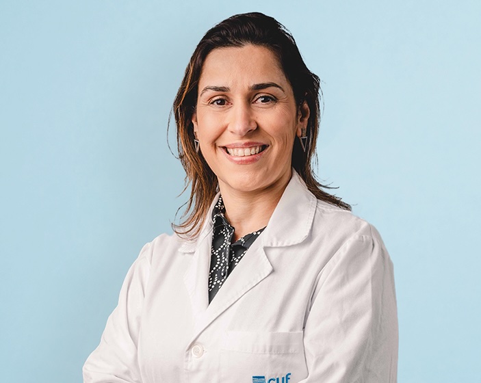 Smiling female healthcare professional in a white lab coat against a light blue background.