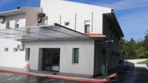 White two-story building with a glass entry door under a metal canopy and a red curb along the front.