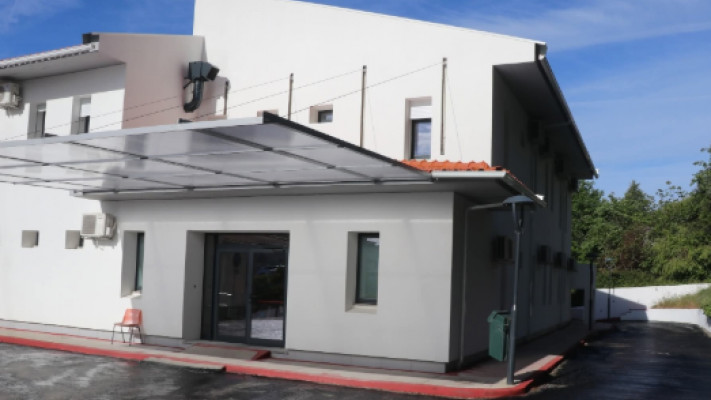 White two-story building with a glass entry door under a metal canopy and a red curb along the front.
