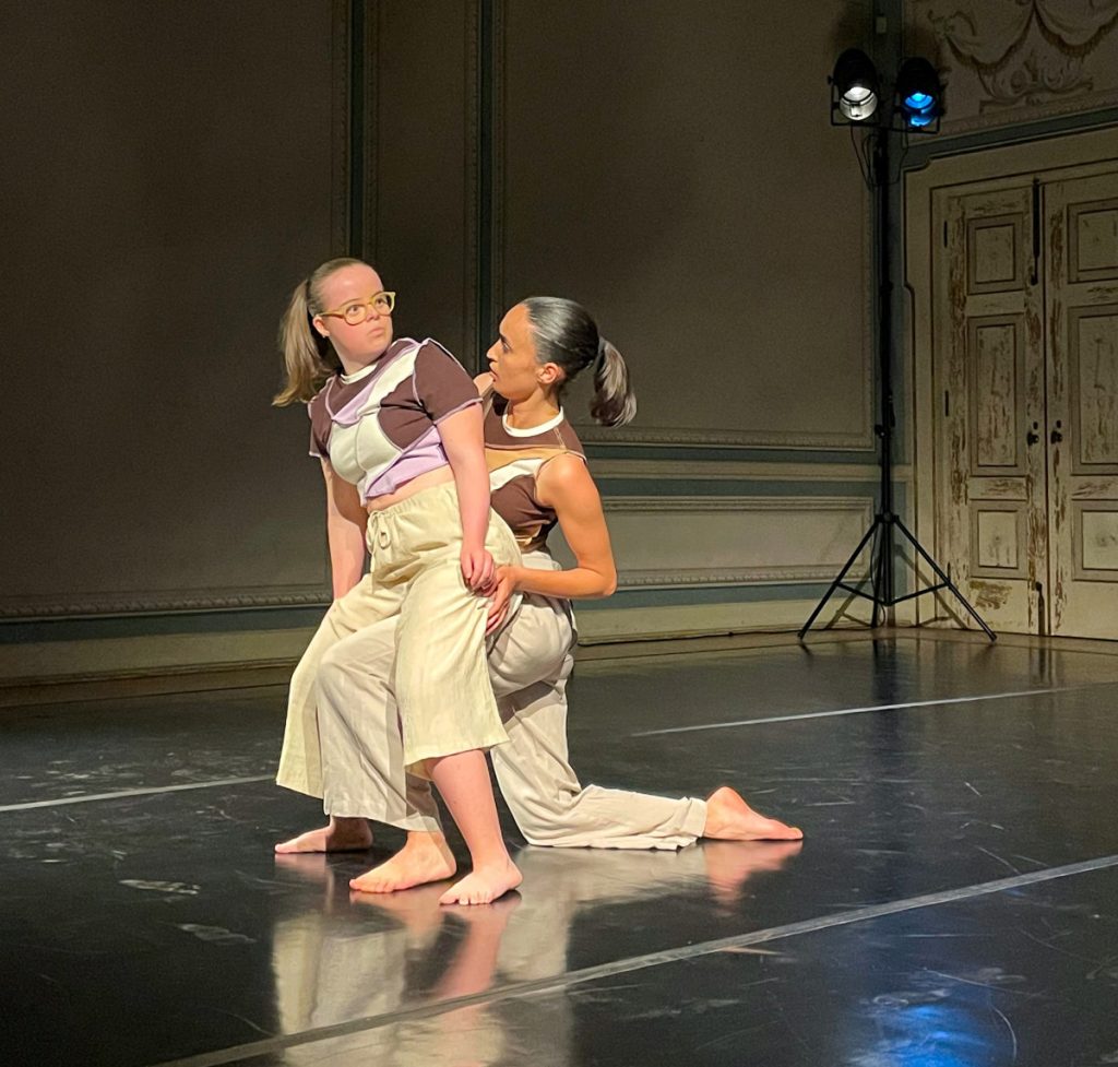 Two female dancers perform a contemporary routine on a stage; one wears pastel crop top and beige pants, the other behind in a similar outfit, both barefoot. CiM e João Cardoso vencem open call da segunda edição da WARM-UP do Teatro Viriato
