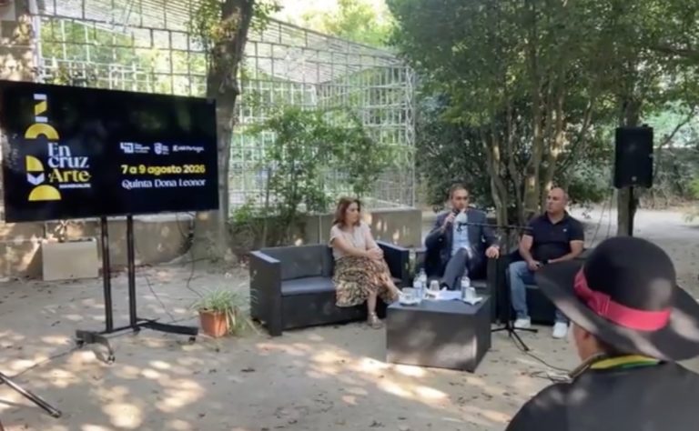 Outdoor panel discussion with three speakers seated on black sofas; a large screen displays event graphics in Spanish on the left.