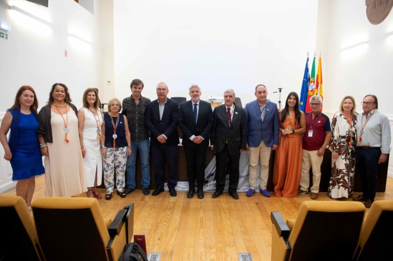 Fifteen people in a row posing for a group photo in a conference room with flags in the background.