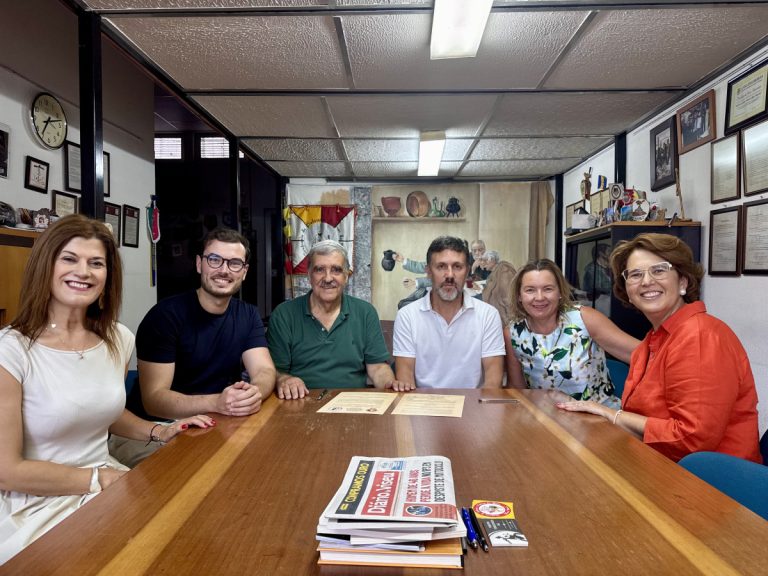 Six adults sit around a wooden conference table, smiling for the camera in a meeting room.