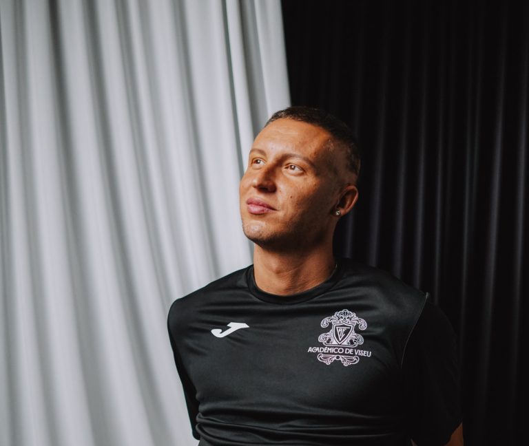 Portrait of a man in a black athletic shirt looking upward, against light and dark curtain backdrop.