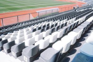 Empty stadium seating with alternating gray and white seats overlooking a green field and red track edge of the stands.