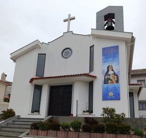 White church facade with a cross on the roof and a bell tower on the right side.