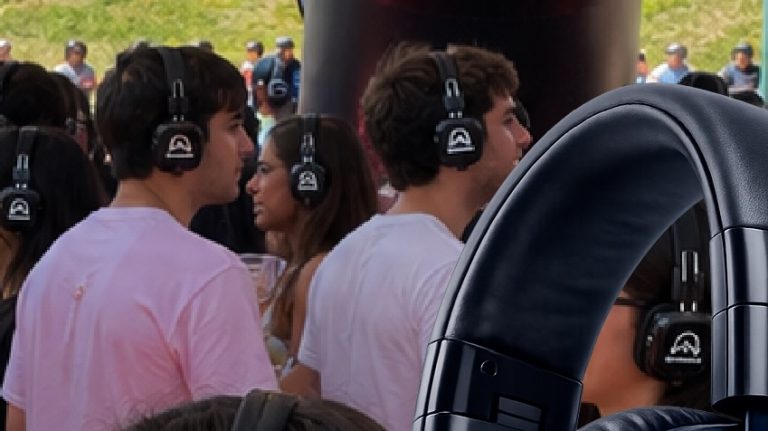 People wearing over-ear headphones at an outdoor listening event, with a large headset prop in the foreground.