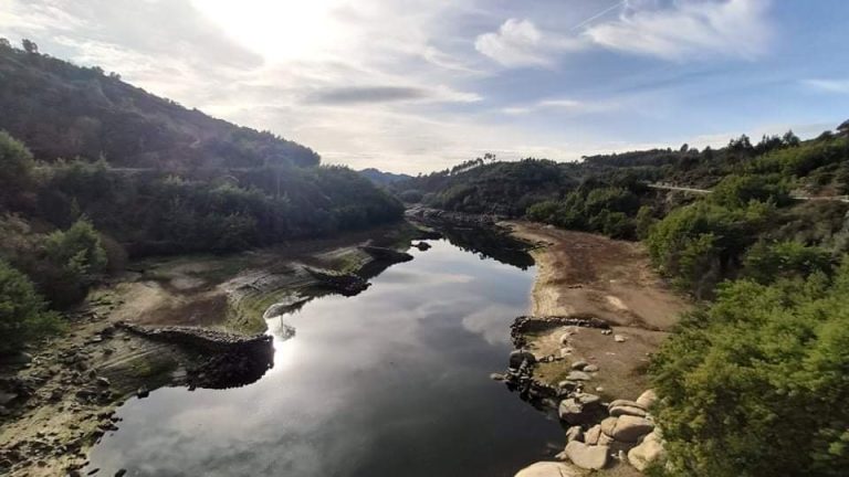 Scenic river winding through rocky banks and green hills under a bright sky with reflection on calm water.