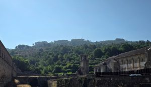 Ruined stone buildings along a hillside with a small bell tower and clear blue sky behind them