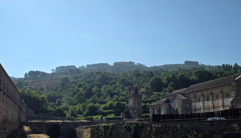 Ruined stone buildings along a hillside with a small bell tower and clear blue sky behind them