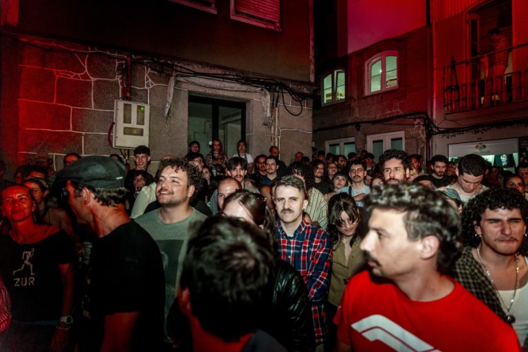 A dense crowd of people at a nighttime outdoor event bathed in red light, facing the camera.