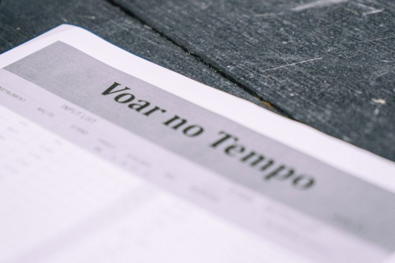 Close-up of a printed page showing the bold title 'Voltar no Tempo' on a gray banner, resting on a dark surface.