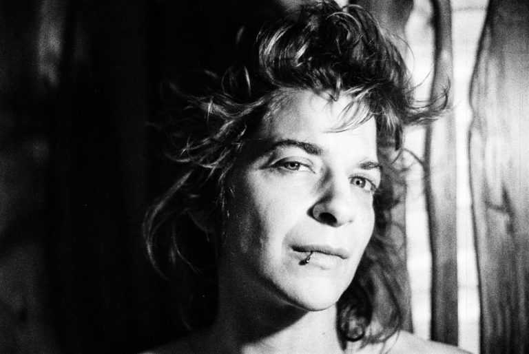 Black-and-white portrait of a person with a lip piercing and tousled hair, looking slightly toward the camera.
