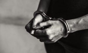 Close-up of hands in metal handcuffs around the wrists, in black-and-white.