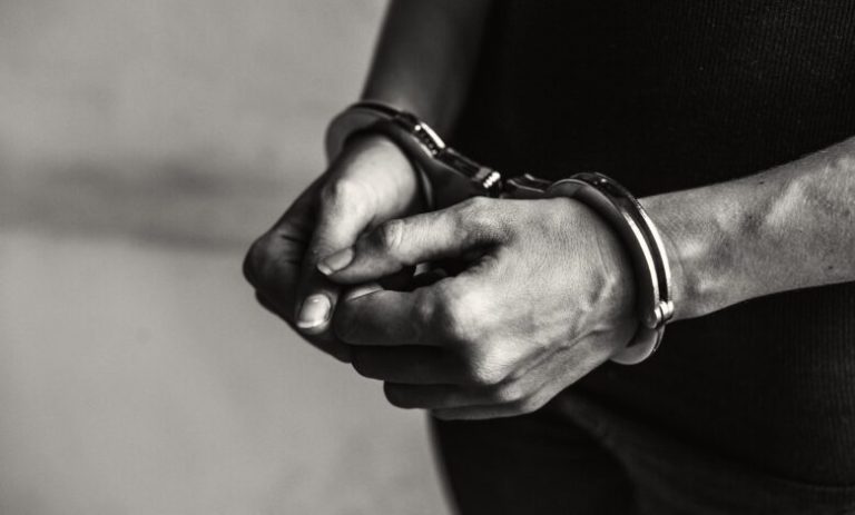 Close-up of hands in metal handcuffs around the wrists, in black-and-white.