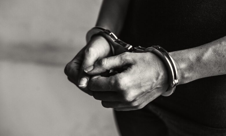Close-up of hands in metal handcuffs around the wrists, in black-and-white.