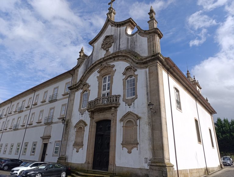 White historic church with ornate stone facade, arched doorway and balcony against a blue sky