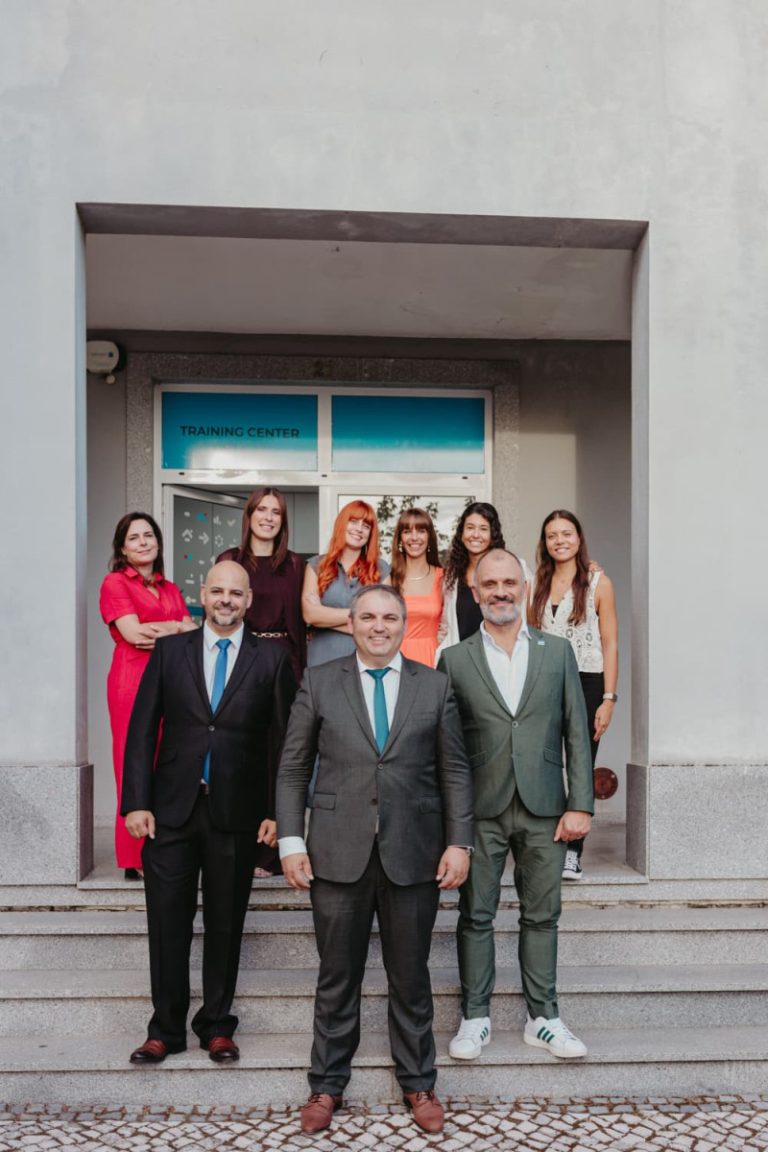 Group of eight professionals in business attire standing on the entrance stairs of a building labeled Training Center, posing for a team photo.